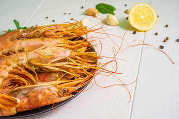 Shrimps prepared for frying on a black glass plate, lemon slices, side view
