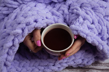 Cup of hot chocolate into woman arms on knitted plaid.