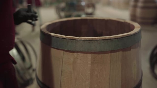 Barrel maker hammering metal hoop in place on top rim of barrel, close up