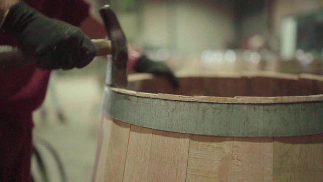 Barrel maker hammering staves in place inside metal hoops, close up