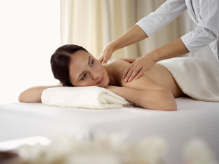 Fototapeta na wymiar Pretty brunette woman enjoying procedure of back massage in spa salon. Beauty concept