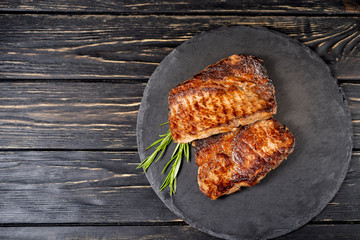 juicy piece of fried meat lies on a stone plate against a black wooden table