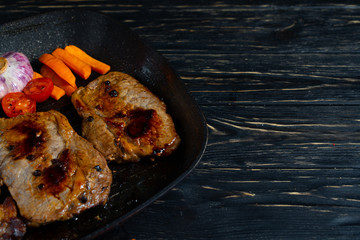 Juicy piece of fried meat in a pan that stands on a black wooden table background