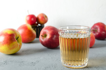 Lot of ripe tasty apples adn glass of apple juice on the grey surface against white wall