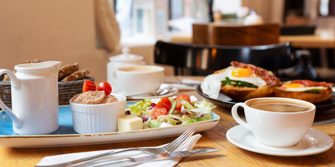 Fototapeta na wymiar Breakfast in restaurant in the morning with coffee cup. Colorful healthy meal with fish spread, tomatoes and salad. Bright indoors with window. Panoramic banner.