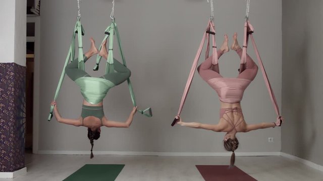 Two aerial yoga female teachers showing elements of a workout falling down in a head down position