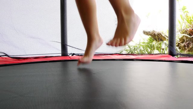 Little kid feet jumping and bouncing at trampoline in slow motion. Close up shot.