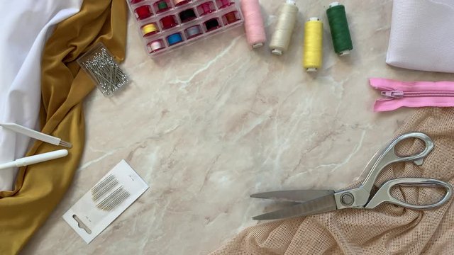 Sewing supplies: cutting scissors, fabric, threads, needles, measuring tape, lightning - appear on the table and come to life - they begin to move. Stop motion, top view.