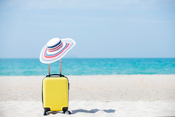 Yellow Suitcase with sun hat on the beach