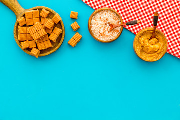 Prepare salted caramel. Scoop with sweet cubes, melted caramel and salt on blue background top view copy space