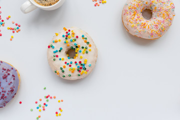 Cups of espresso coffee and sweet donuts decorated colorful sprinkles on white background. Flat lay. Top view. Unhealthy food