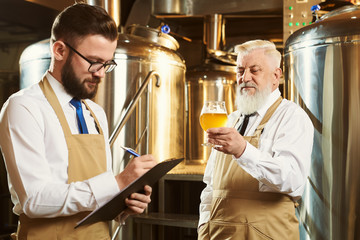 Two workers of brewery examining craft beer.