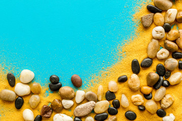 Resort or vacation concept. Sea stones and sand on blue background top-down frame copy space