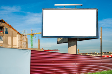 Blank billboard for advertisement on the construction site with cranes on a sunny day.
