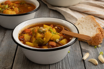 Carrot, potato and bell pepper vegan soup served in enameled bowls with bread, garlic on a rustic wooden background