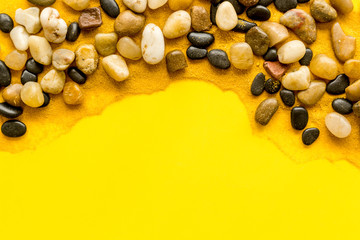 Sea rest, summer vacation concept. Stones and sand on yellow background top-down frame copy space