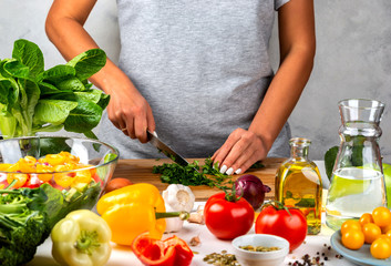 Woman cuts greens and cooking salad in the kitchen. Healthy diet concept.
