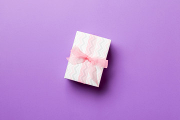 Gift box with pink bow for Christmas or New Year day on purple background, top view with copy space