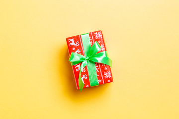 wrapped Christmas or other holiday handmade present in paper with green ribbon on yellow background. Present box, decoration of gift on colored table, top view with copy space