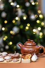 Gingerbread cookies on a wooden plank and teapot in front of christmas tree and blurred lights. White christmas tree decorations. Homemade cookie made with molasses and flavored with ginger.