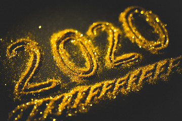 2020 number poured from gold glitters on a dark black table.