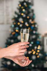 Girl holding two glasses with champagne near a blurred Christmas tree. Concept of holiday party and pleasure. Selected focus with bokeh