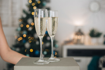 Girl holding two glasses with champagne near a blurred Christmas tree. Concept of holiday party and pleasure. Selected focus with bokeh