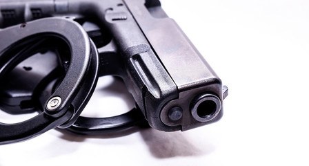 A black 9mm pistol with a set of black handcuffs next to it on a white background