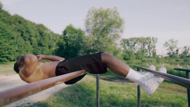 Strong athlete doing sit ups in green park on parallel bars