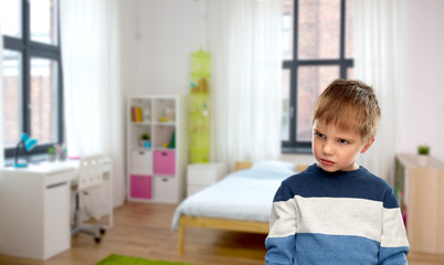 childhood, expressions and people concept - portrait of gloomy little boy in striped pullover over home room background