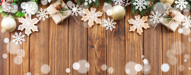 Christmas frame with Christmas gifts, Christmas tree branches, bokeh and snowflake in the shape of a gingerbread cookie on a wooden background. Flat lay style