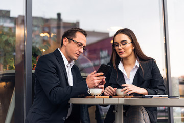 Business people in cafe, working while break. Business-team working on laptop at coffee bar, looking a mobile phone.