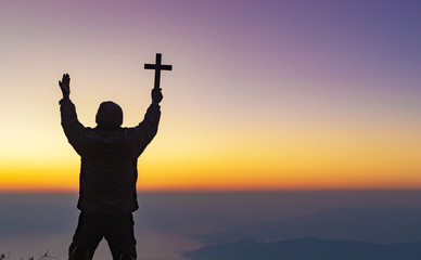 Fototapeta premium Human praying and holding christian cross for worshipping God at sunset sky background.Christian, Christianity, Religion copy space background.