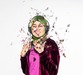 Obraz premium Studio shot, portrait of young beautiful Asian muslim wearing hijab listening to music with headset