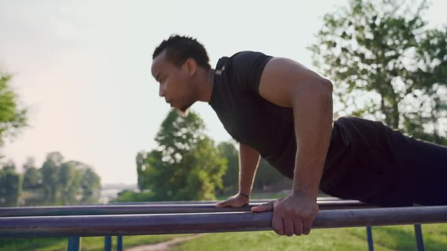 Muscular afro man exercising on outdoor sport equipment