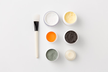 beauty, spa and wellness concept - blue clay mask, body butter and therapeutic mud with brush on white background