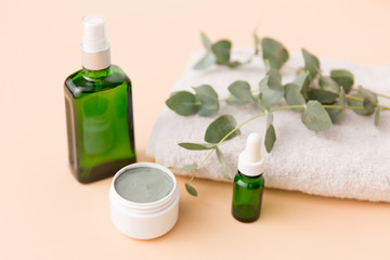 Fototapeta na wymiar beauty, spa and wellness concept - serum, clay mask, oil and eucalyptus cinerea on bath towel