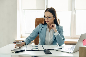 Successful small business owner. Beautiful young businesswoman using laptop and doing some paperwork while working on laptop.