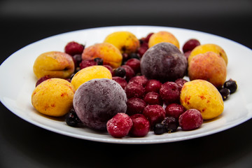 A Berry mix from frozen currant, apricot, plum, cherry on the white plate. Frozen Berries from freezer. A background with frozen plum, currant, apricot and cherry. A healthy Berries on the background