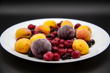 A Berry mix from frozen currant, apricot, plum, cherry on the white plate. Frozen Berries from freezer. A background with frozen plum, currant, apricot and cherry. A healthy Berries on the background