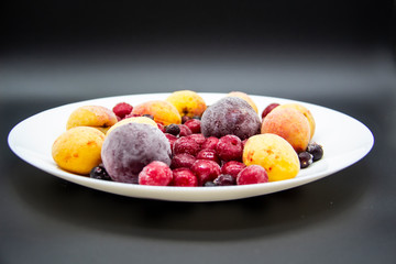 A Berry mix from frozen currant, apricot, plum, cherry on the white plate. Frozen Berries from freezer. A background with frozen plum, currant, apricot and cherry. A healthy Berries on the background