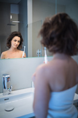 Pretty, middle aged woman brushing her teeth in a modern design bathroom