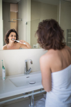 Pretty, Middle Aged Woman Brushing Her Teeth In A Modern Design Bathroom