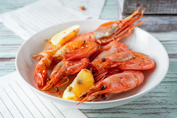 Jumbo prawns with lemon wedges served on white plate, paper napkins on wooden background, closeup view