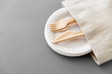 cutlery, recycling and eco friendly concept - wooden forks and knives on paper plates and canvas napkin on grey background