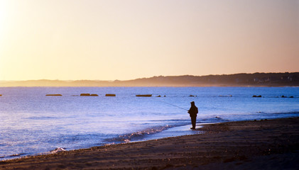 Fototapeta na wymiar A Man in Silhouette on a Beach Fishing
