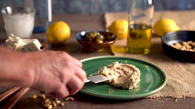 Long clip of beautiful setting of middle eastern food as hand comes in a spreads hummus onto a plate, pours olive oil and sprinkles paprika.