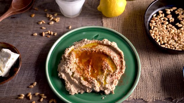 High angle slide to the right of middle eastern food spread with hummus, pine nuts, lemons, olives, get and ouzo or arak.