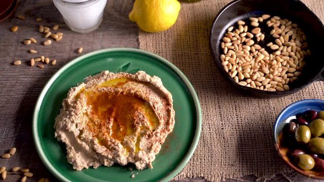 High angle slide to the left of middle eastern food spread with hummus, pine nuts, lemons, olives, get and ouzo or arak.