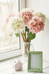 Light pink hydrangea for wedding bouquet in glass vase and photo frame on window background. Mother's day or March 8 greeting card template. Spring card concept. Beautiful bouquet of flowers in vase